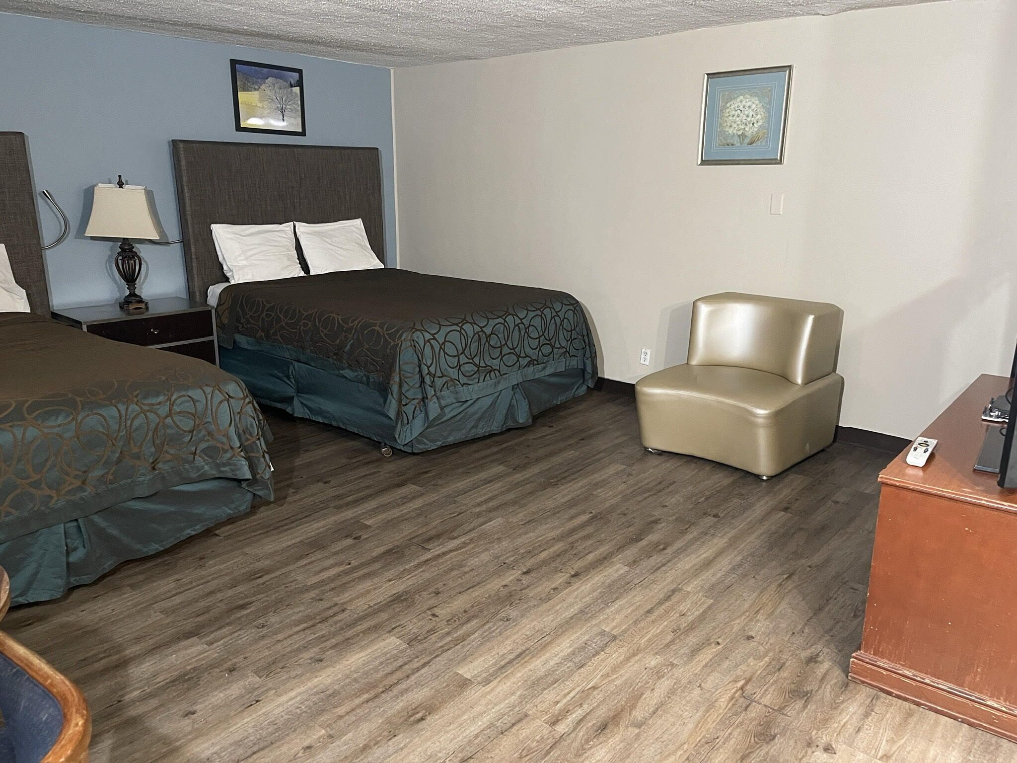 A hotel room with two beds, a chair, a desk, and a lamp.