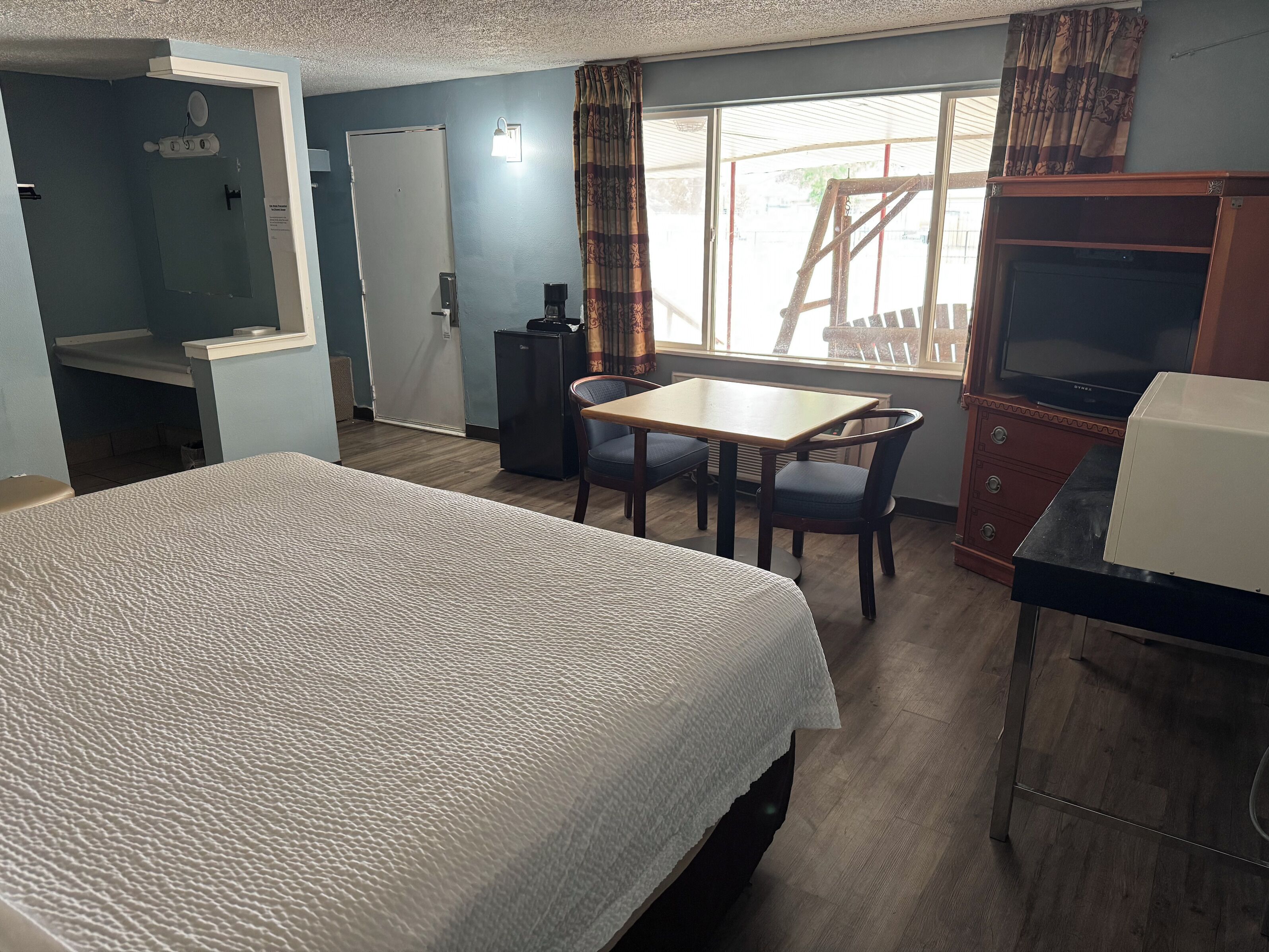 A hotel room with a large bed, a small table with chairs, a television, and a wardrobe.
