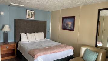 A hotel room with a bed, a nightstand, a lamp, a framed picture on the wall, and a sofa.
