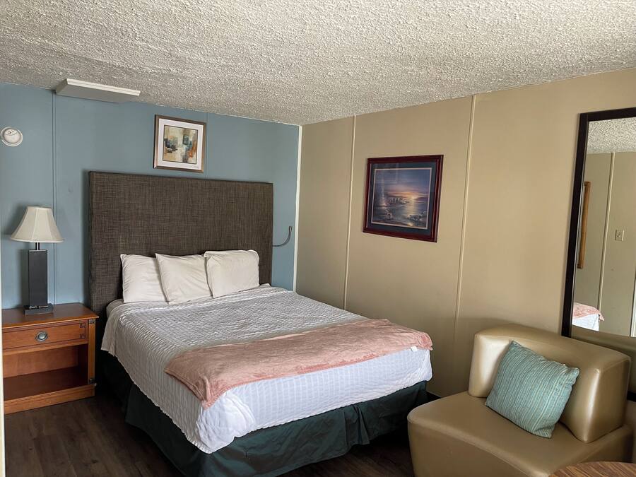 A hotel room with a bed, a nightstand, a lamp, a framed picture on the wall, and a sofa.