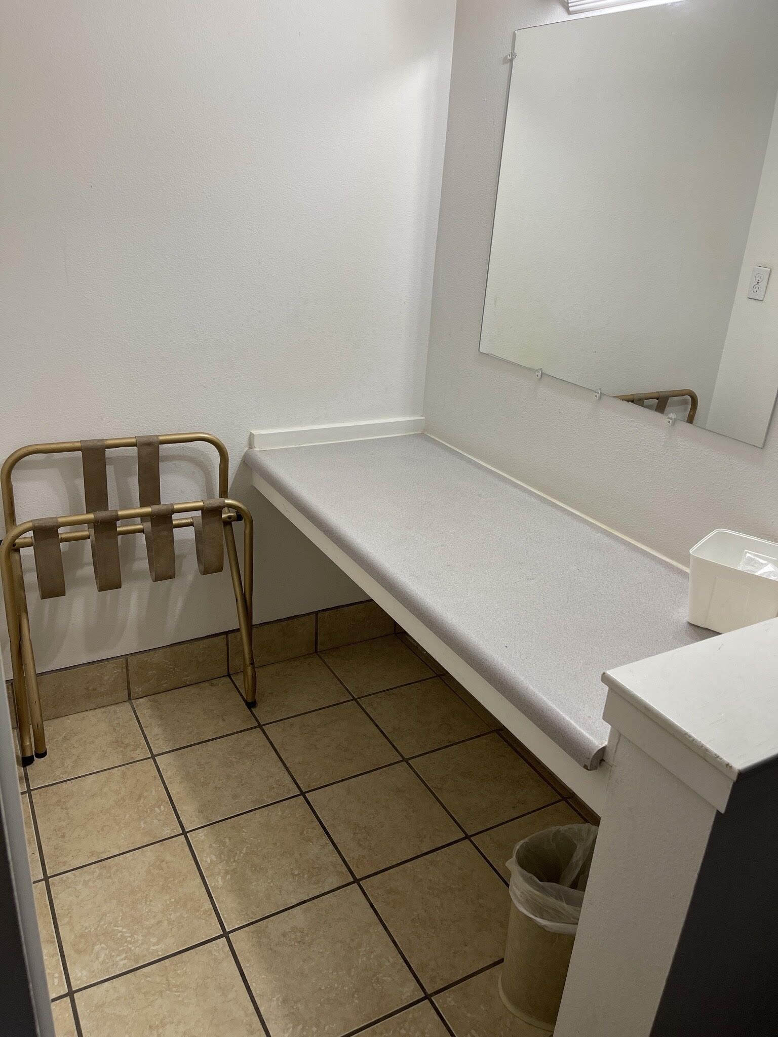 A small bathroom with a white countertop, a mirror, a towel rack, and a trash can.
