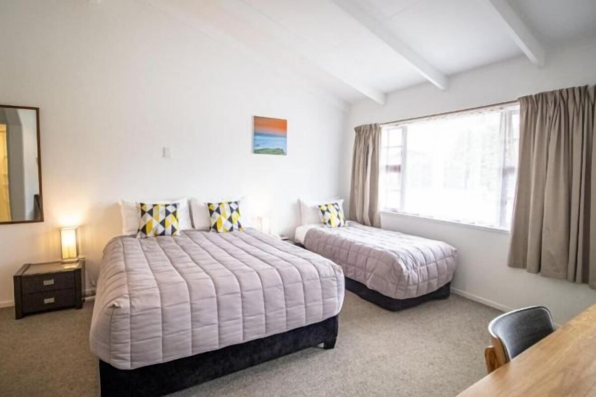 A bedroom with two beds, a nightstand, a desk, and a window with curtains.
