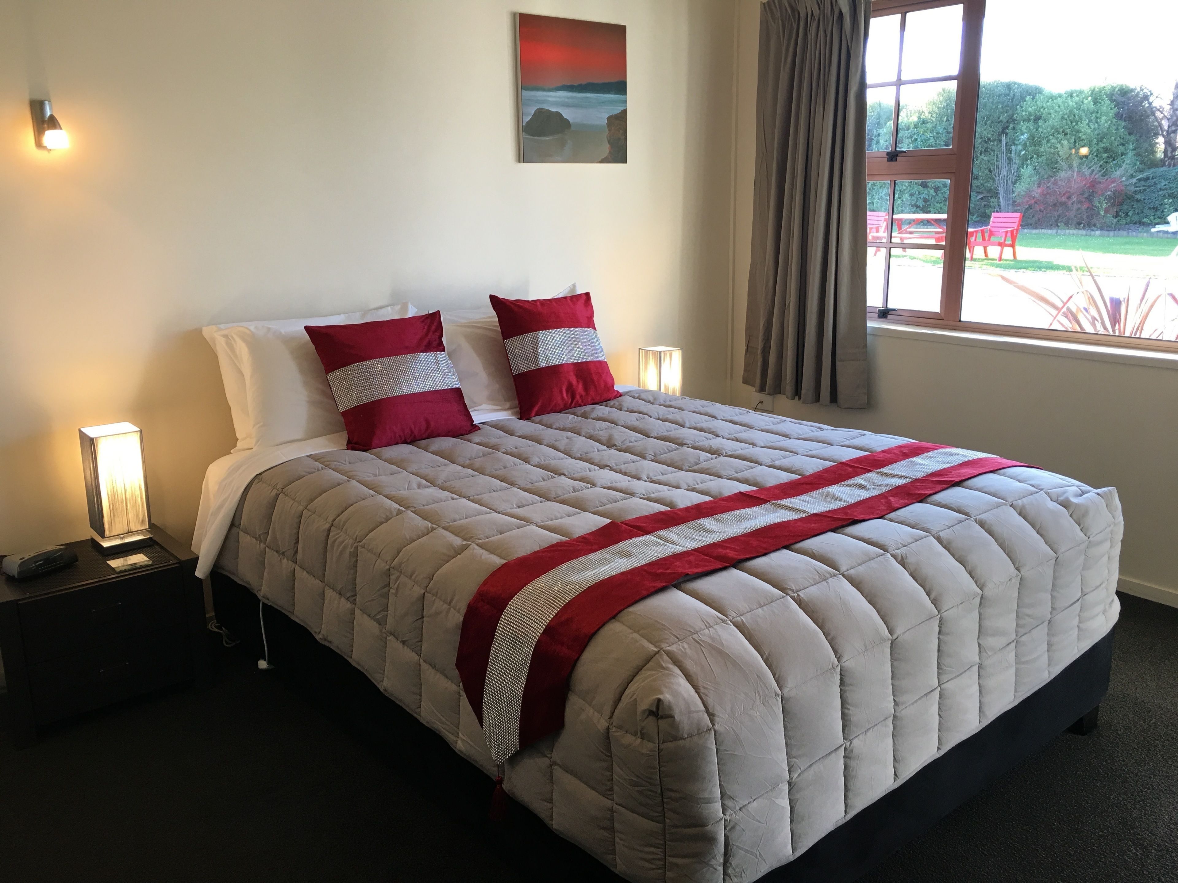 A neatly made bed with a quilted headboard, two pillows with reflective stripes, and a red accent.
