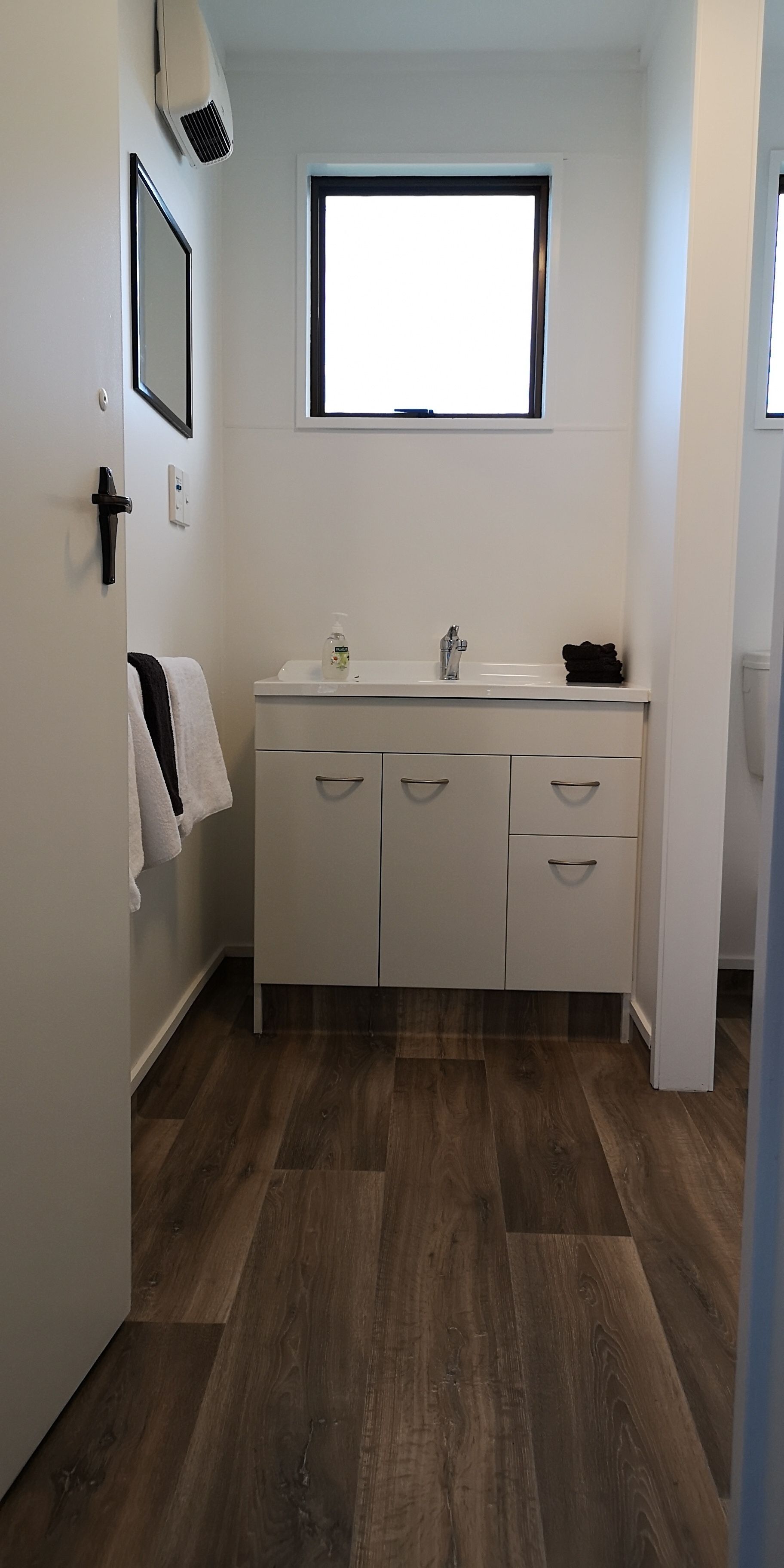 A small, clean bathroom with a white sink, a mirror, and a window above the sink.