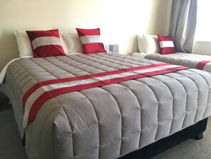 Una cama con colcha gris, almohadas rojas y una manta a rayas blancas y rojas, además de un cabecero blanco.