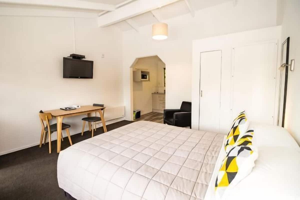 Quarto com cama, escrivaninha, cadeira, televisão e porta.