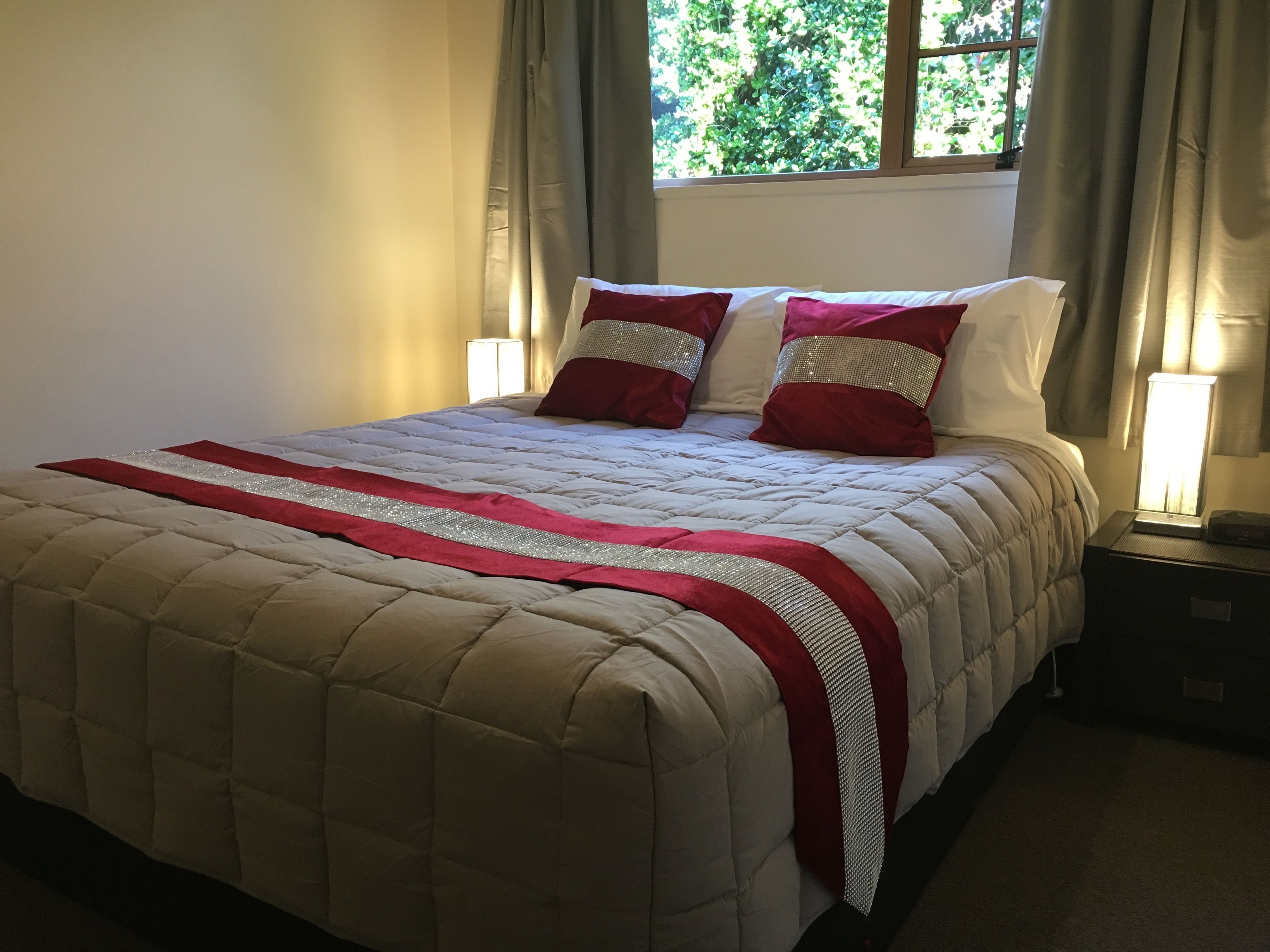 Un lit bien fait, avec une couverture matelassée et des coussins décoratifs, une lampe de chevet et une fenêtre avec des rideaux.