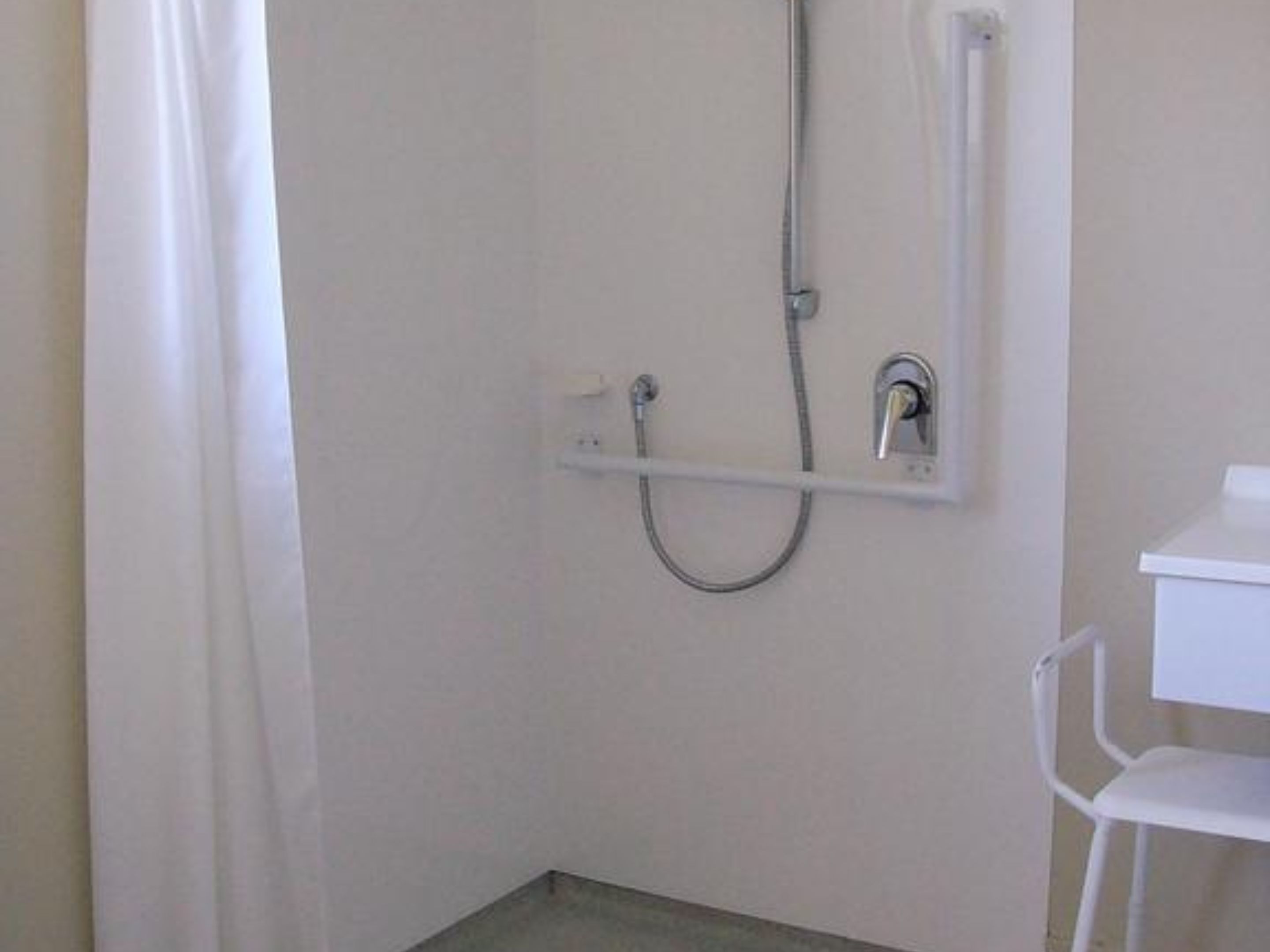 Ein kleines, weißes Badezimmer mit Dusche, einem weißen Stuhl und einem weißen Regal.