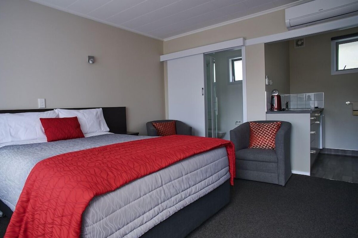 Una habitación de hotel con cama, escritorio, silla, kitchenette y puerta corredera.