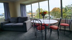 Una sala moderna con un sofá gris, una mesa de comedor redonda con sillas tapizadas en rojo y un jarrón con flores.