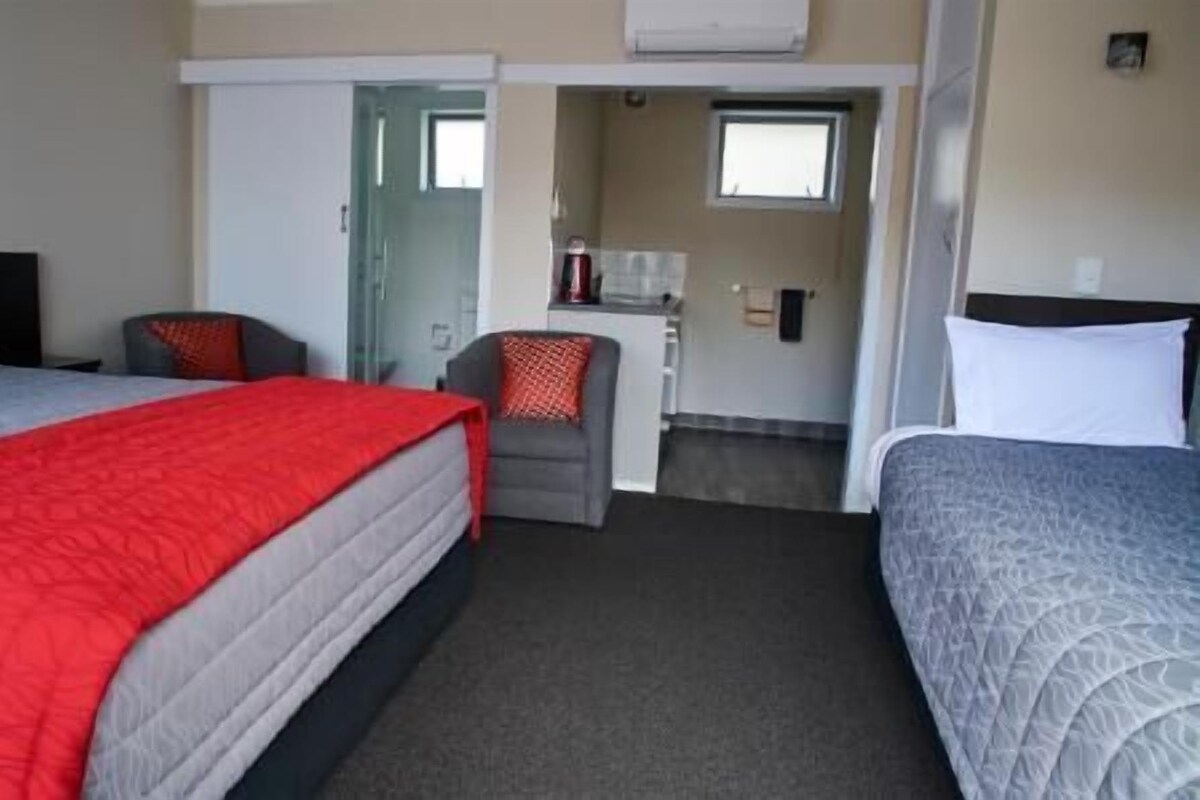 A hotel room with two beds, a small kitchenette, and a bathroom.