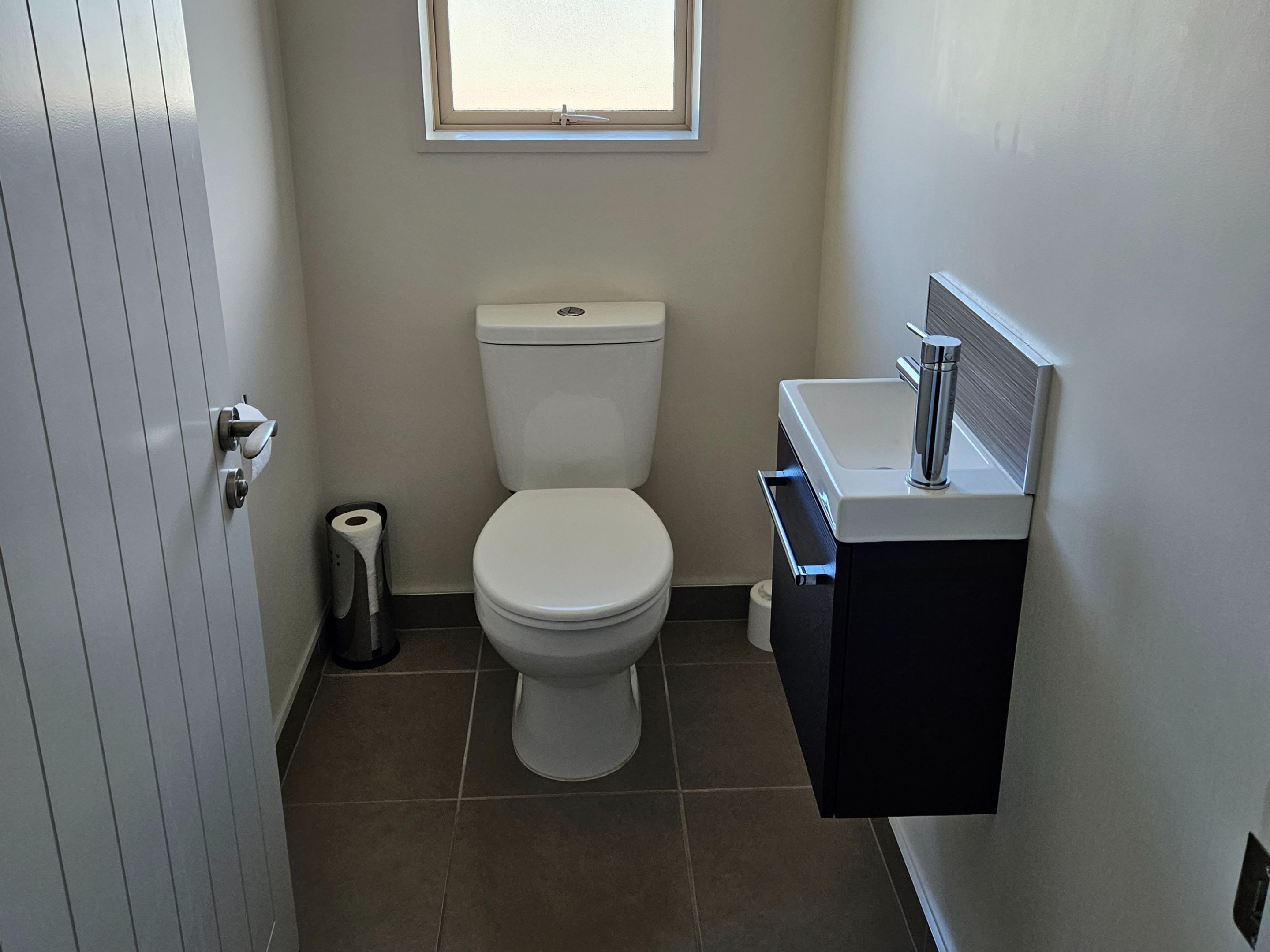 Un baño pequeño y limpio con inodoro, lavabo y ventana sobre el inodoro.