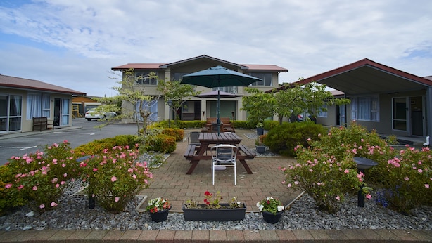 Un hotel con zona de patio que incluye una mesa y sillas, rodeado de plantas y flores en macetas.