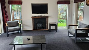 Una sala de estar con chimenea, un televisor montado sobre ella y dos sofás. Hay una mesa pequeña en el centro y una ventana a la izquierda.