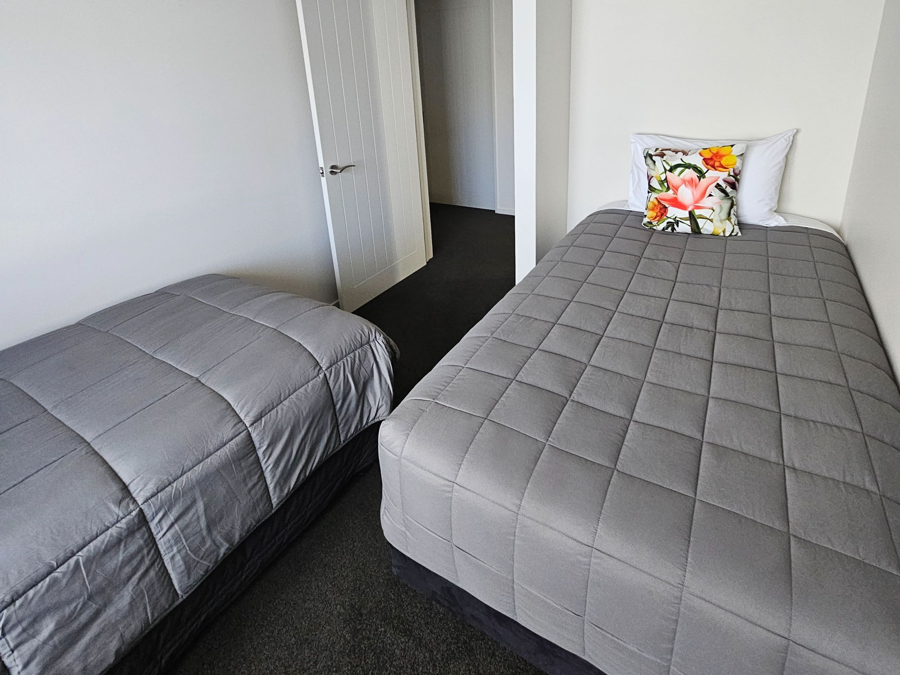 A room with two single beds, each with a grey quilted duvet and a floral pillow.