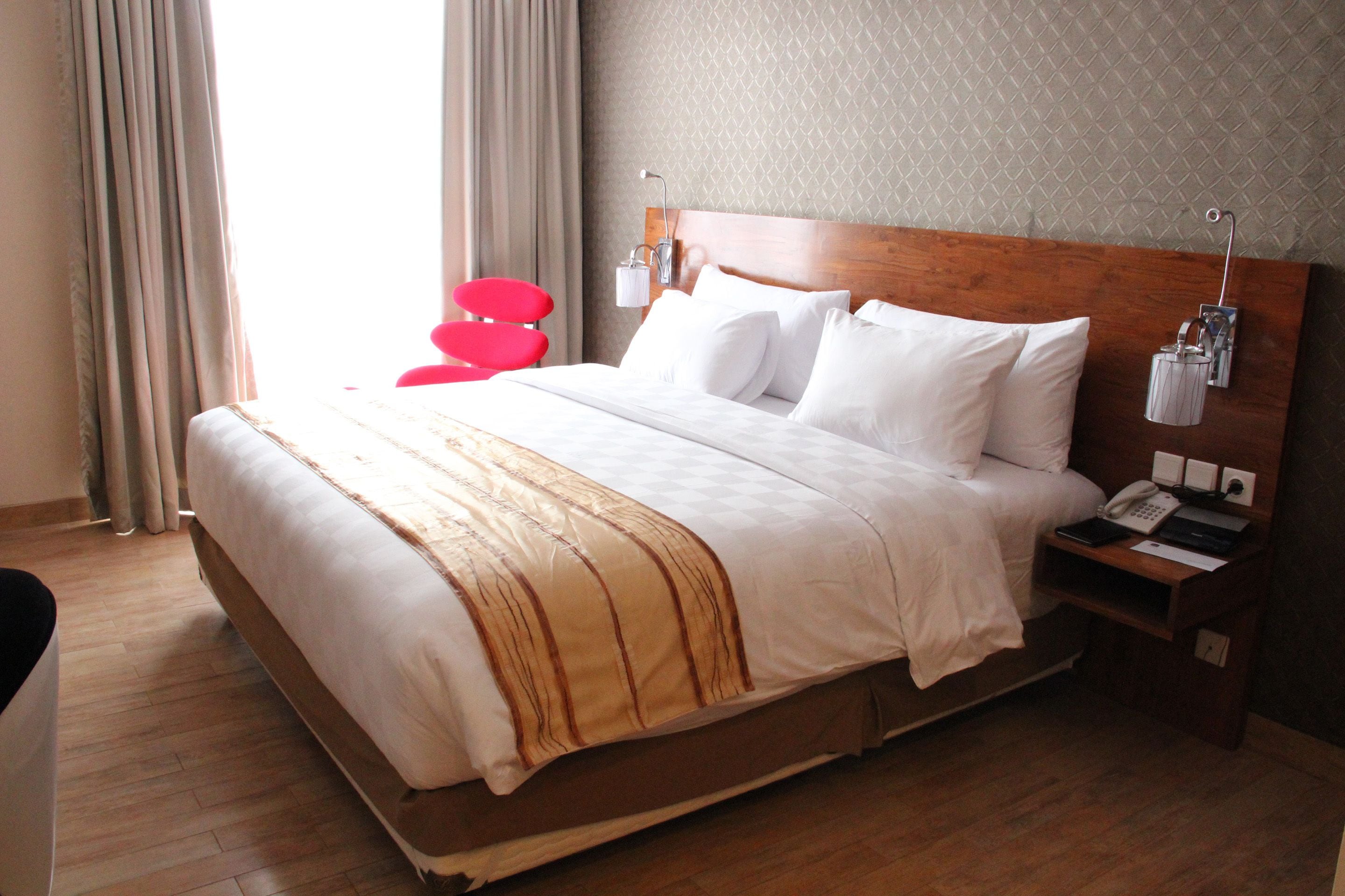 Une chambre d’hôtel avec un grand lit, une tête de lit en bois, des tables de chevet avec des lampes et un fauteuil rouge.