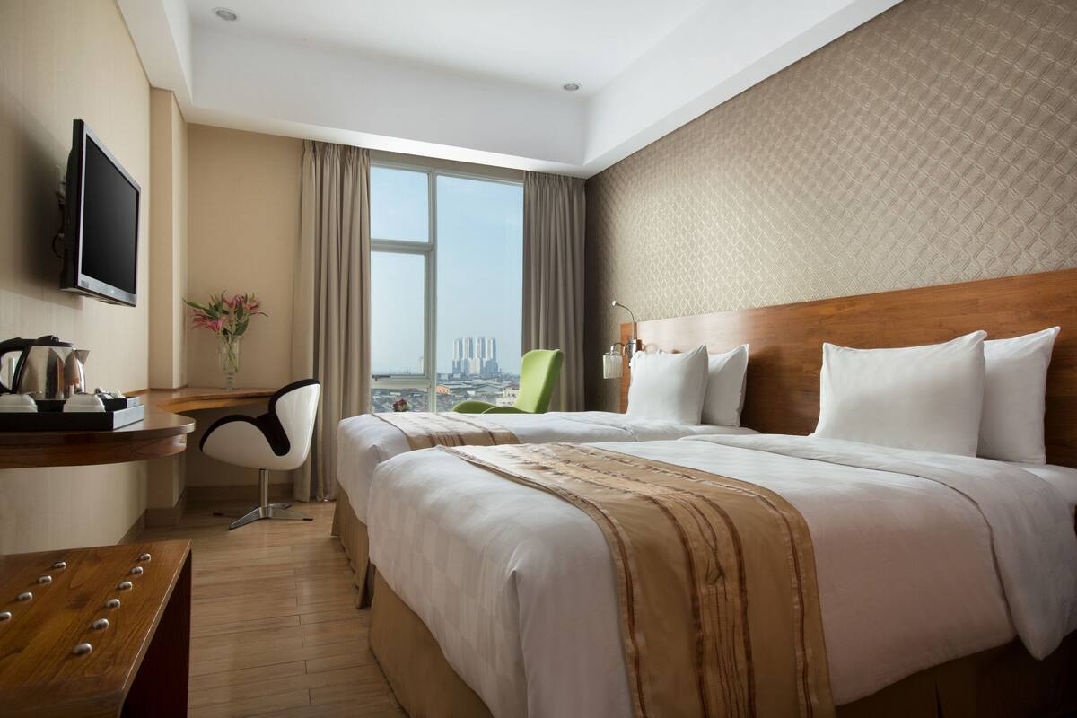 A hotel room with a large bed, a desk with a chair, a TV, and a view of a cityscape.
