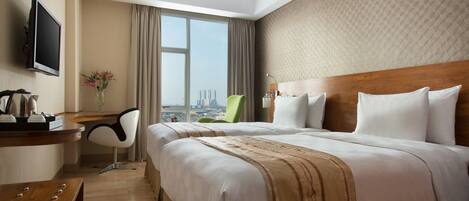 A hotel room with a large bed, a desk with a chair, a TV, and a view of a cityscape.