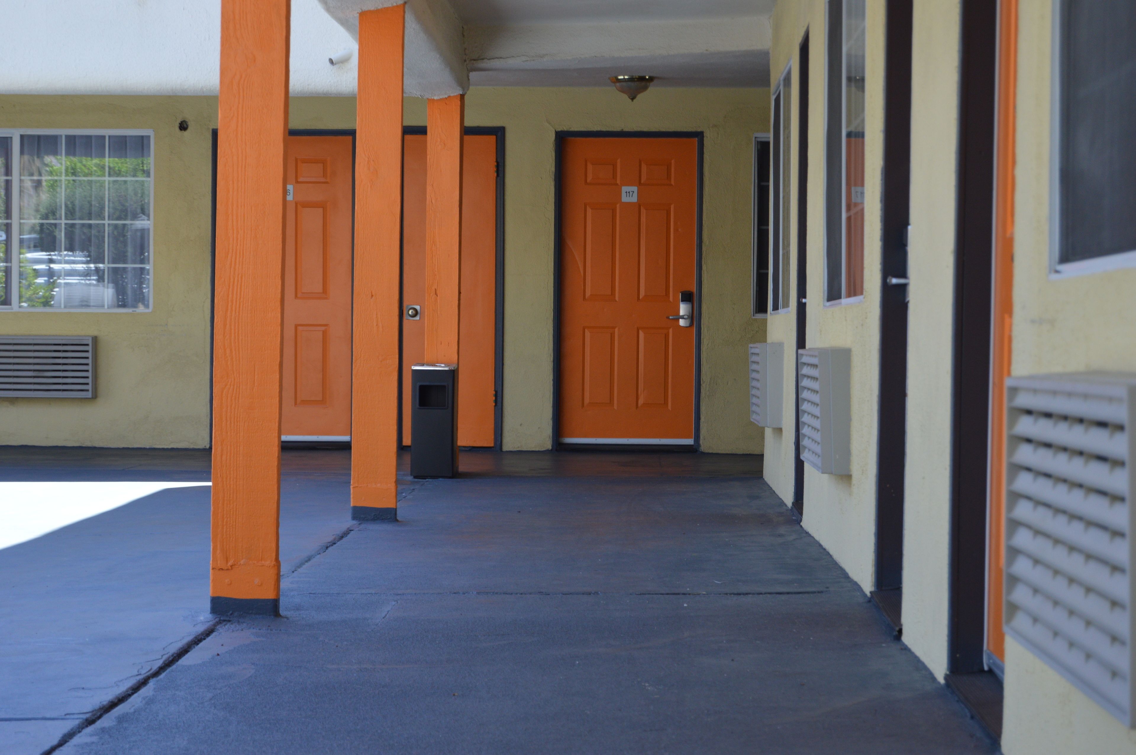 Une entrée d’immeuble avec des portes orange, un sol en béton et une fenêtre avec des stores.