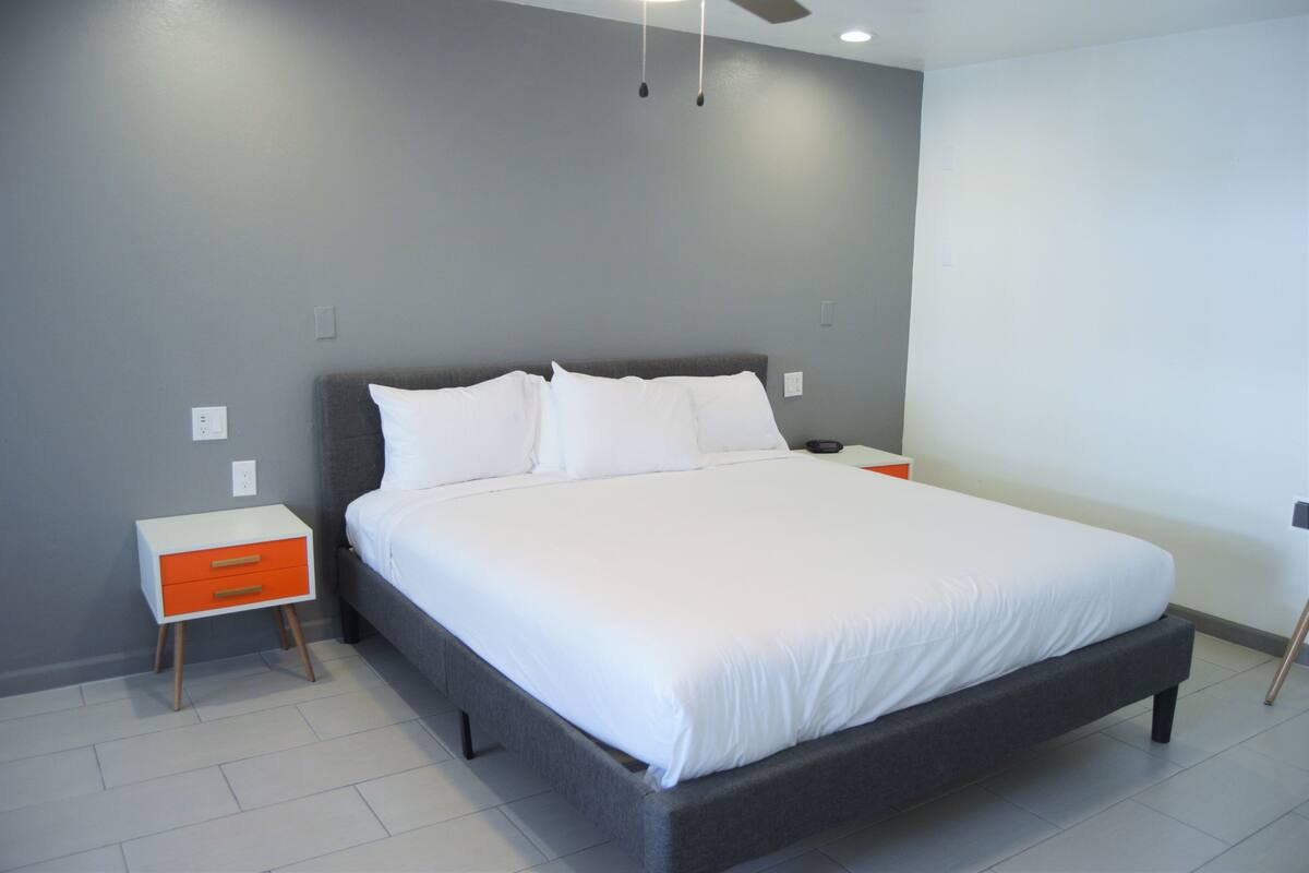 A modern bedroom with a large bed, a nightstand with a drawer, and a ceiling fan.
