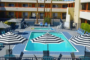 A hotel pool area with multiple lounge chairs and striped umbrellas, a small pool, and a staircase leading to the building. - Musicland Hotel (Palm Springs)
