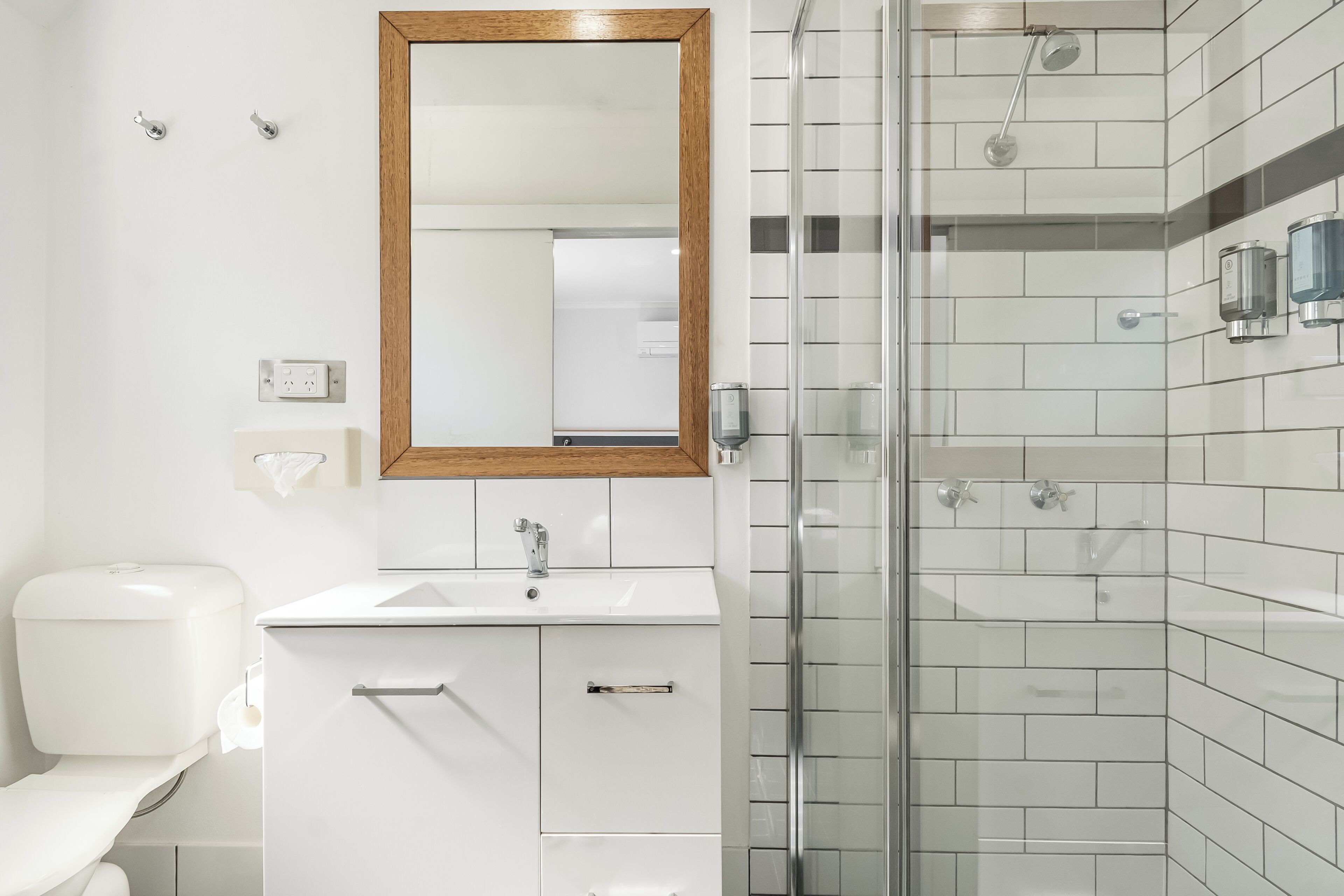 A modern bathroom with a white sink, mirror, and toilet, a glass shower enclosure, and tiled walls.