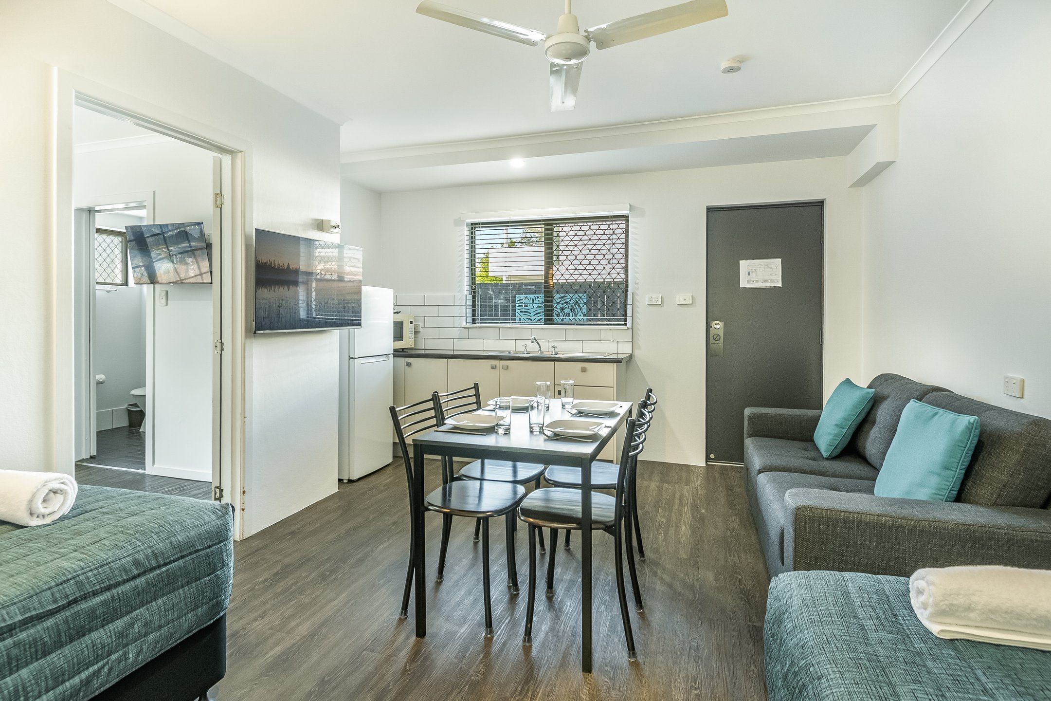 Een knus woongedeelte met een kitchenette, een eethoek en een zithoek met een bank en twee stoelen.