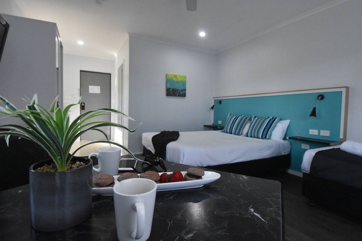 A hotel room with a bed, bedside table, and a potted plant.