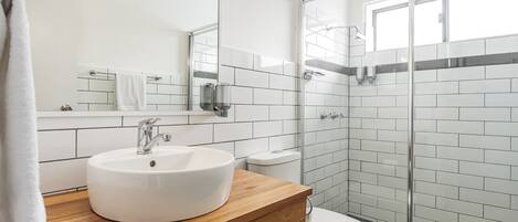 A modern bathroom with a white sink, a mirror, a toilet, and a glass shower enclosure.