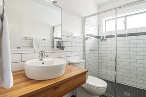 A modern bathroom with a white sink, a mirror, a toilet, and a glass shower enclosure. - Ballina Homestead Motel (Ballina)