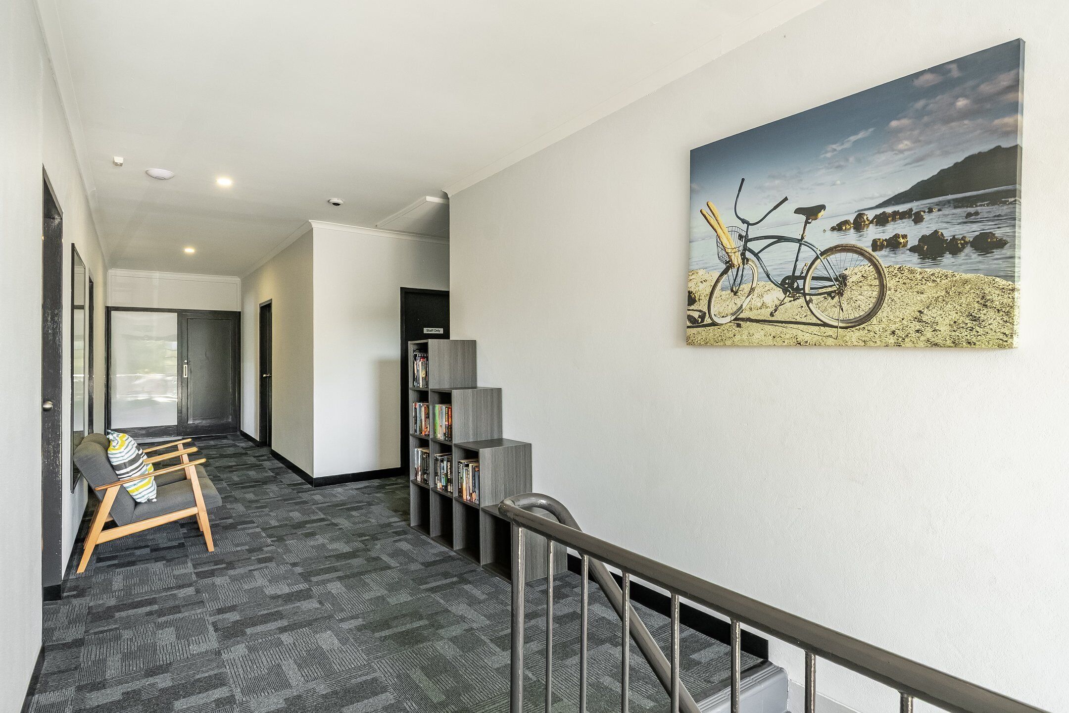 A hallway with a staircase, a bookshelf, and a bicycle leaning against the wall.