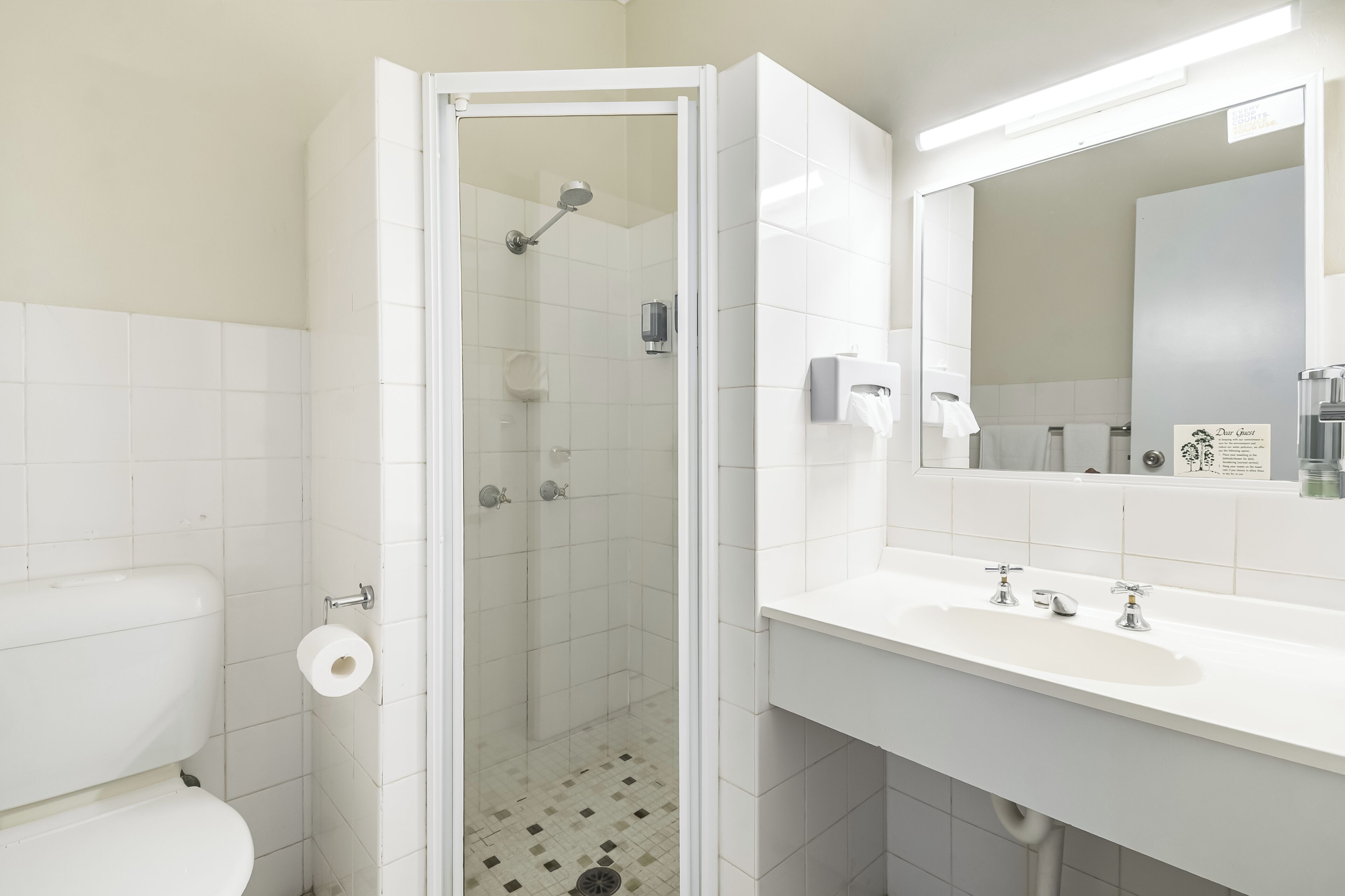 A bathroom with a toilet, a shower with a glass door, a sink with a mirror, and a tiled floor.