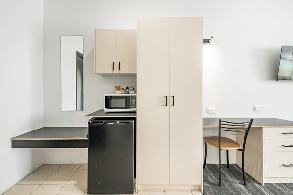 Una cocina compacta con microondas, refrigerador y una silla de madera.