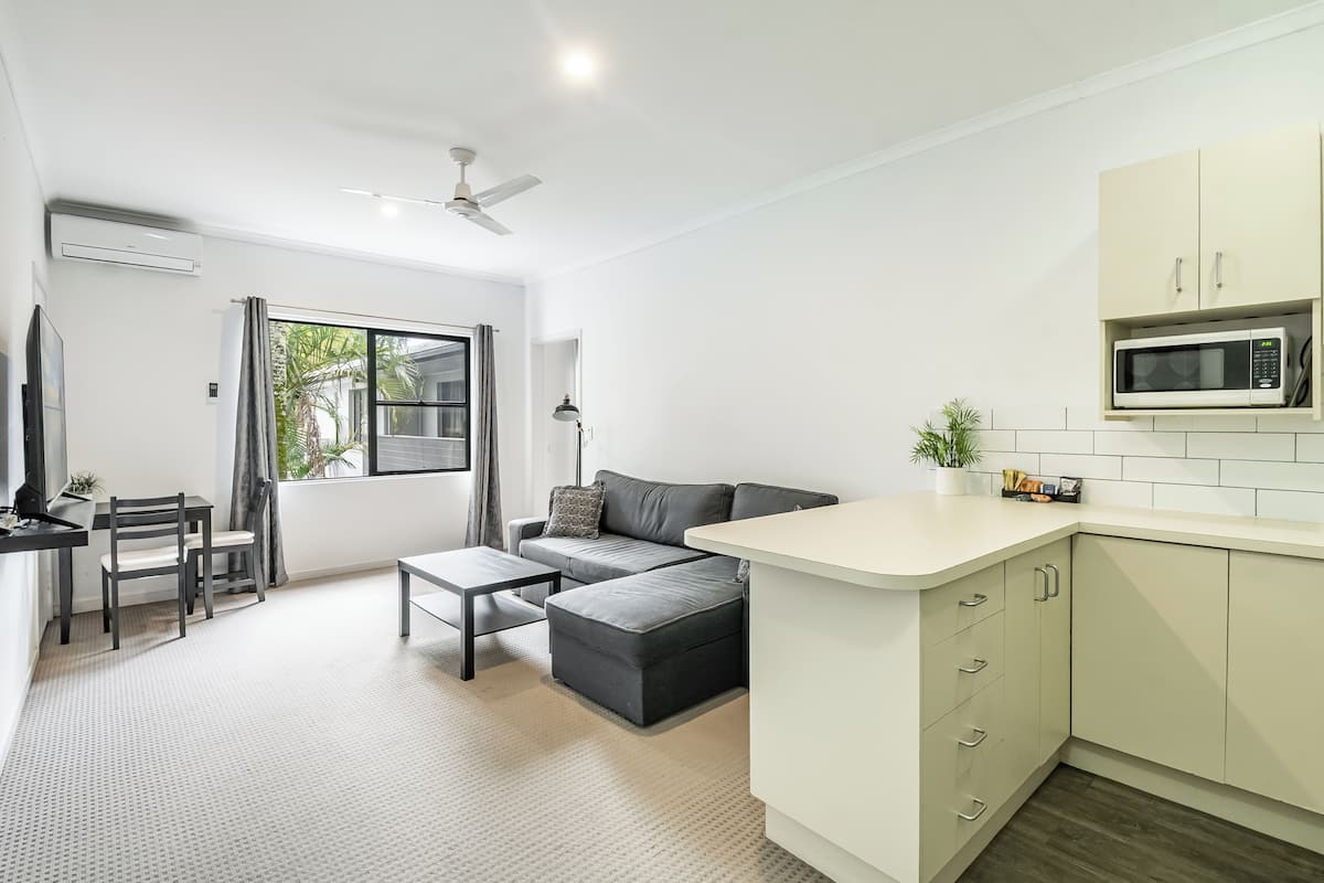 A modern kitchen with a microwave, a dining area with a table and chairs, and a grey sofa.