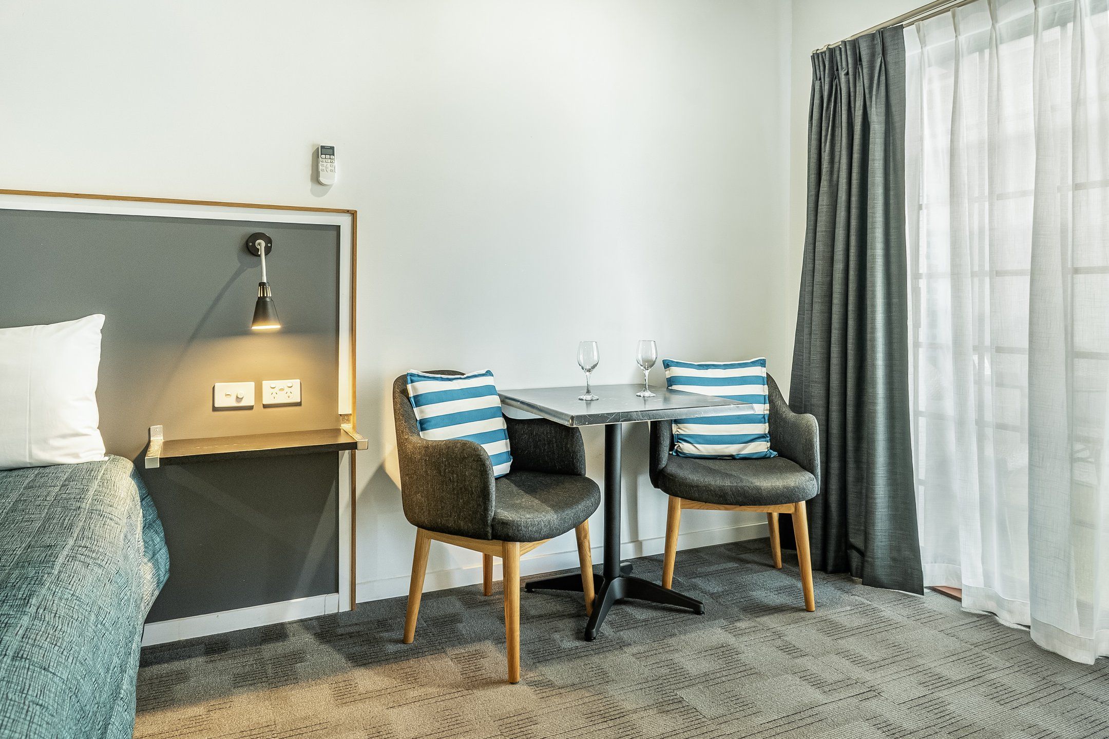 Una habitación de hotel con una cama, un escritorio con dos sillas, una lámpara y una ventana con cortinas.
