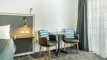 Una habitación de hotel con una cama, un escritorio con dos sillas, una lámpara y una ventana con cortinas.