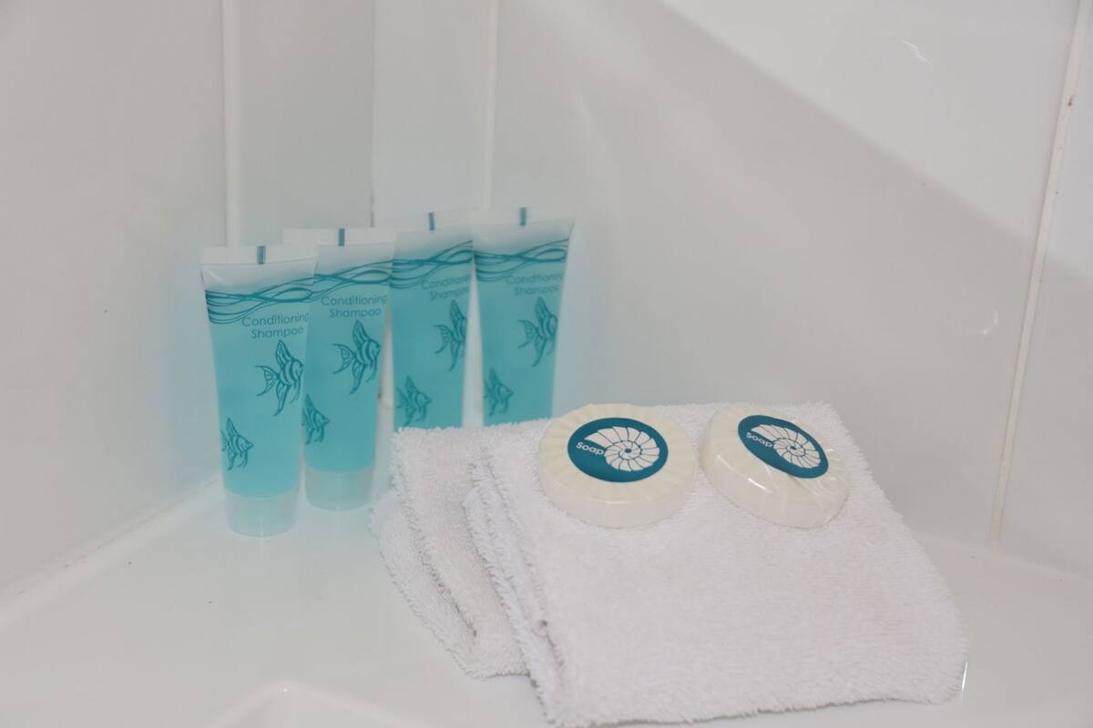 A bathroom with a white sink, a white towel, and three bottles of conditioning shampoo.