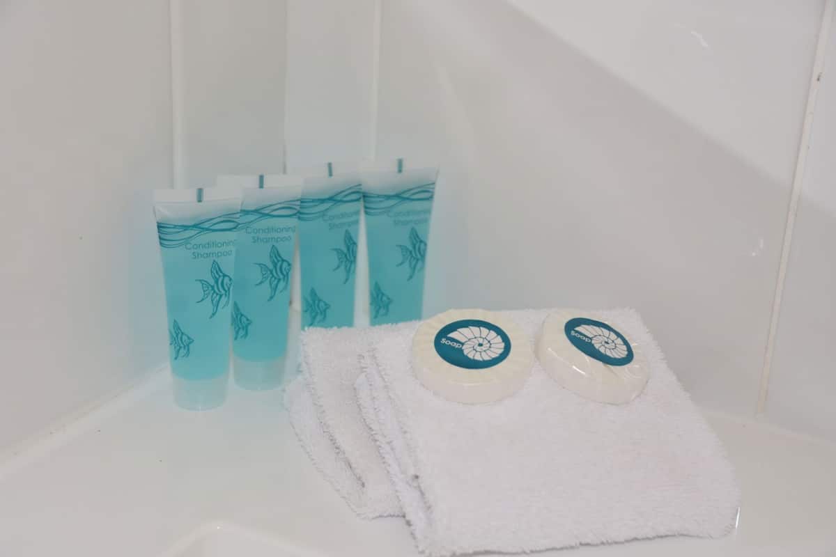 Ein Badezimmer mit einem weißen Waschbecken, einem weißen Handtuch und drei Flaschen mit Conditioner-Shampoo.