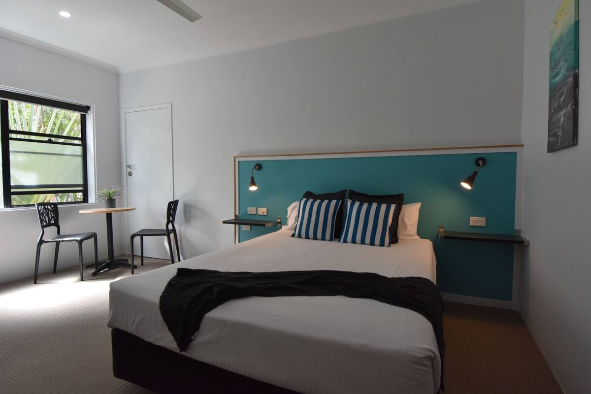 A modern bedroom with a large bed, a desk, two chairs, and a window.