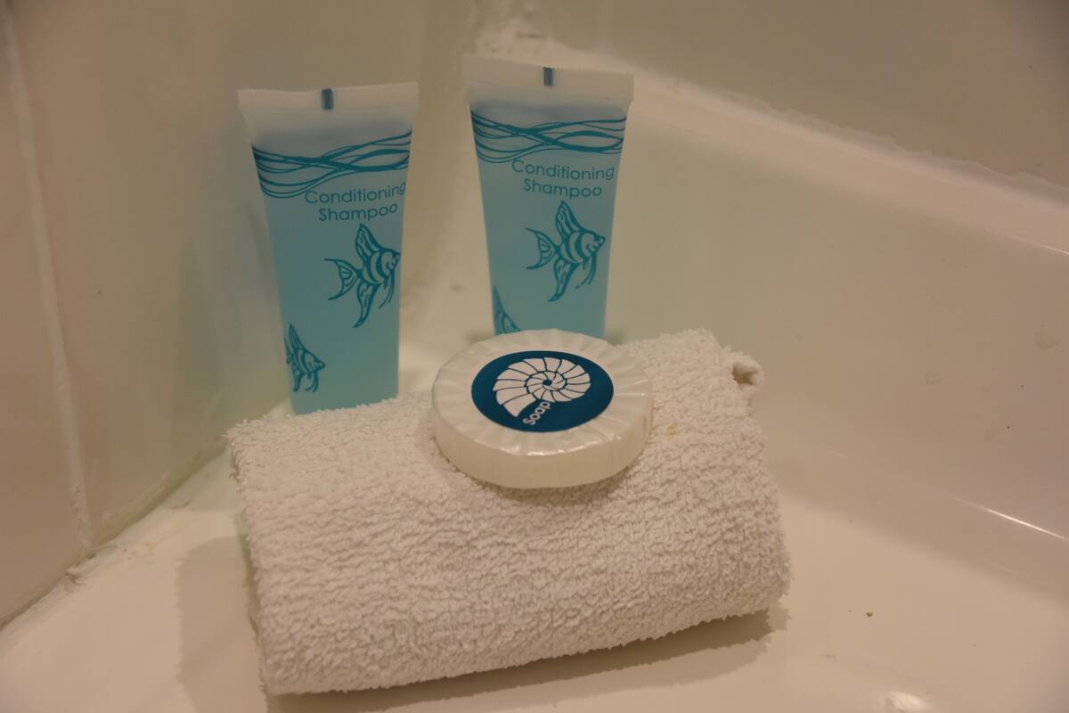 A bathroom with a white bathtub, two bottles of conditioning shampoo, and a white towel with a soap dish.