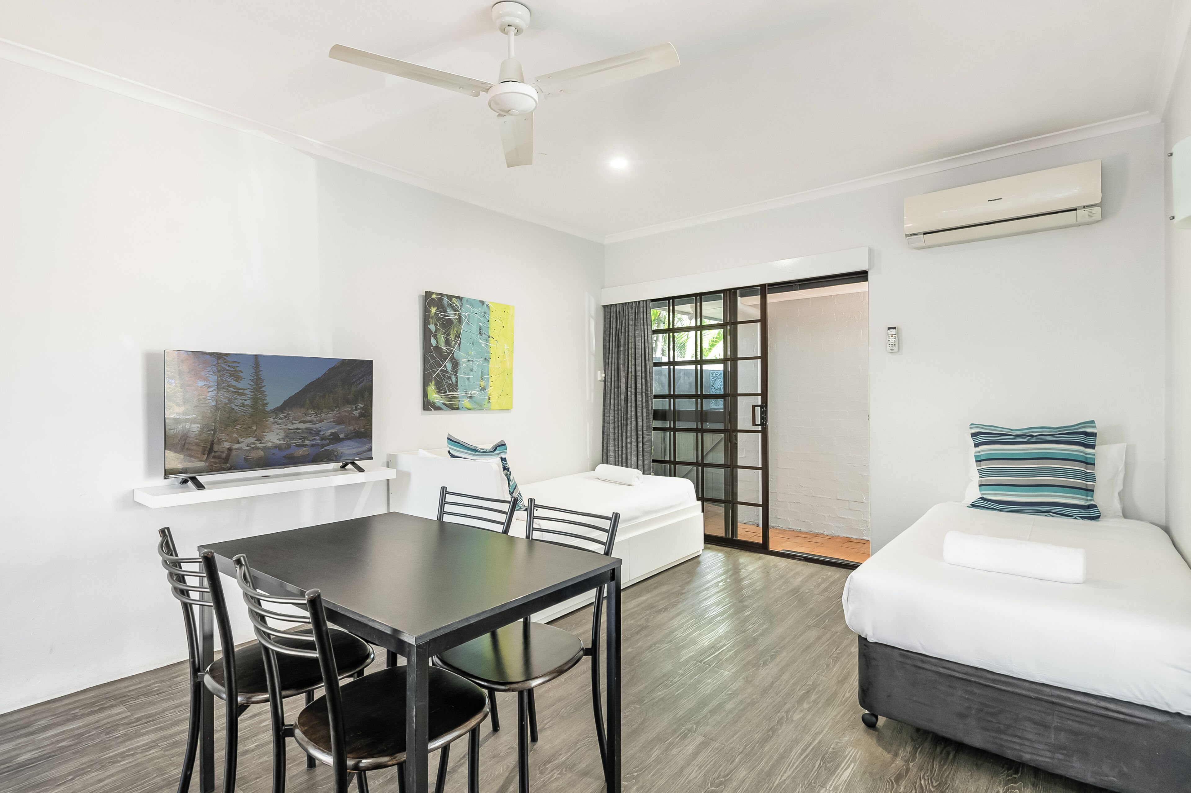 A modern room with a dining table, chairs, a sofa, a TV, and an air conditioning unit.