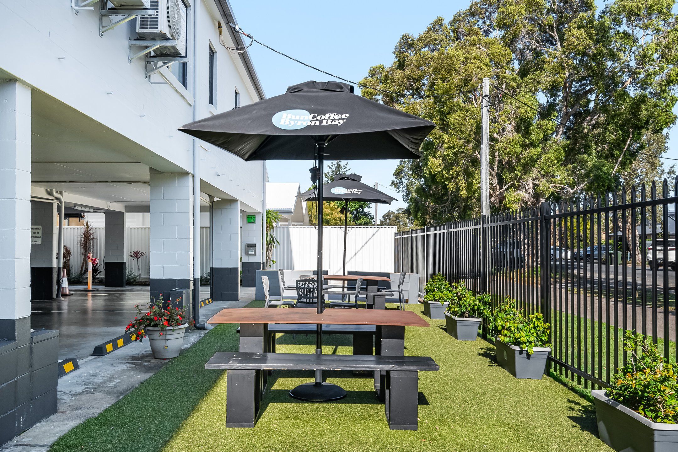 An outdoor seating area with a table and chairs under a canopy, surrounded by a fence and greenery.