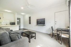 Ein modernes Wohnzimmer mit einer Couch, einem Couchtisch, einem an der Wand befestigten Fernseher und einem Essbereich mit Stühlen.