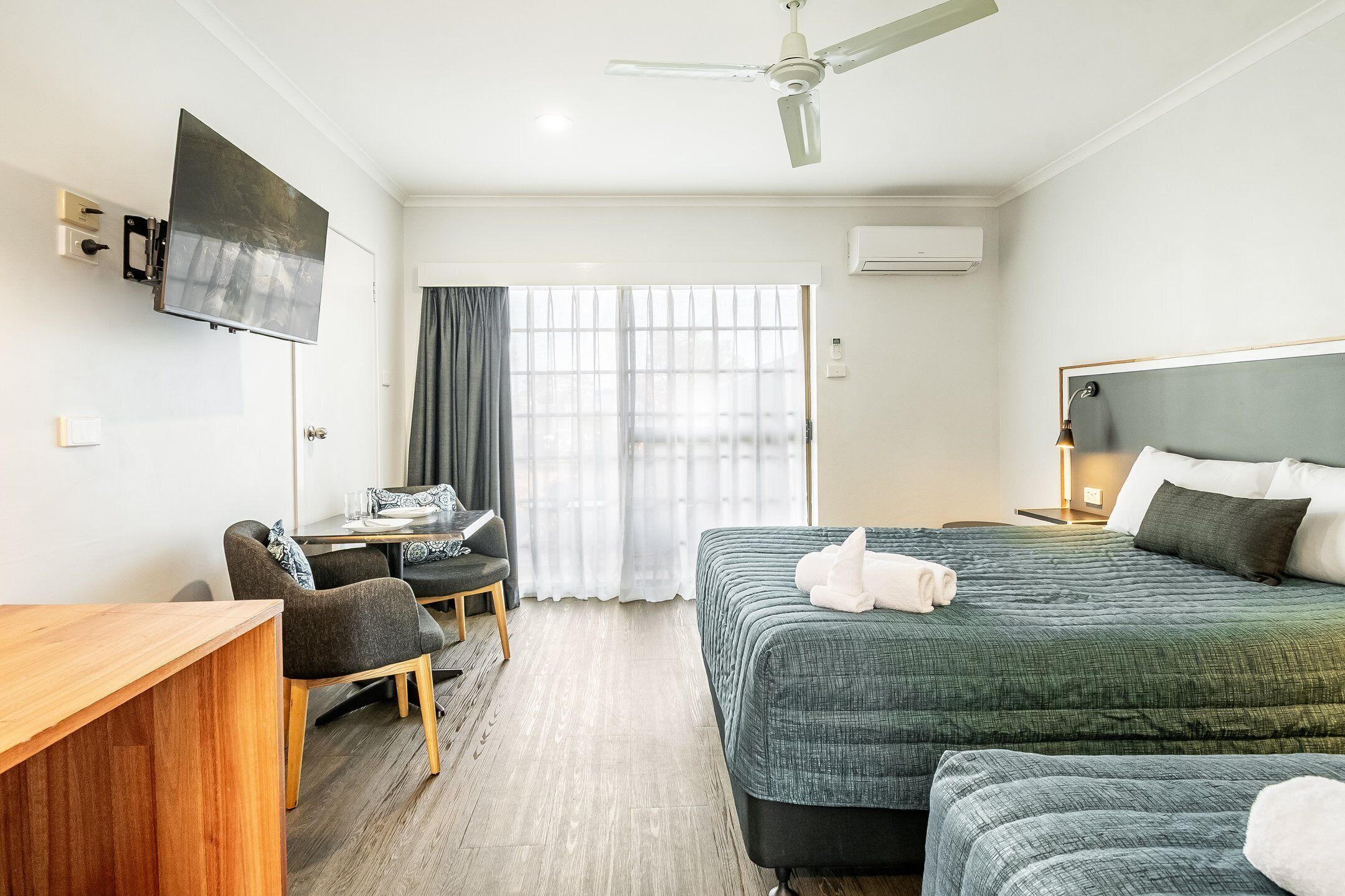 A hotel room with a bed, a desk, a chair, a television, and a ceiling fan.