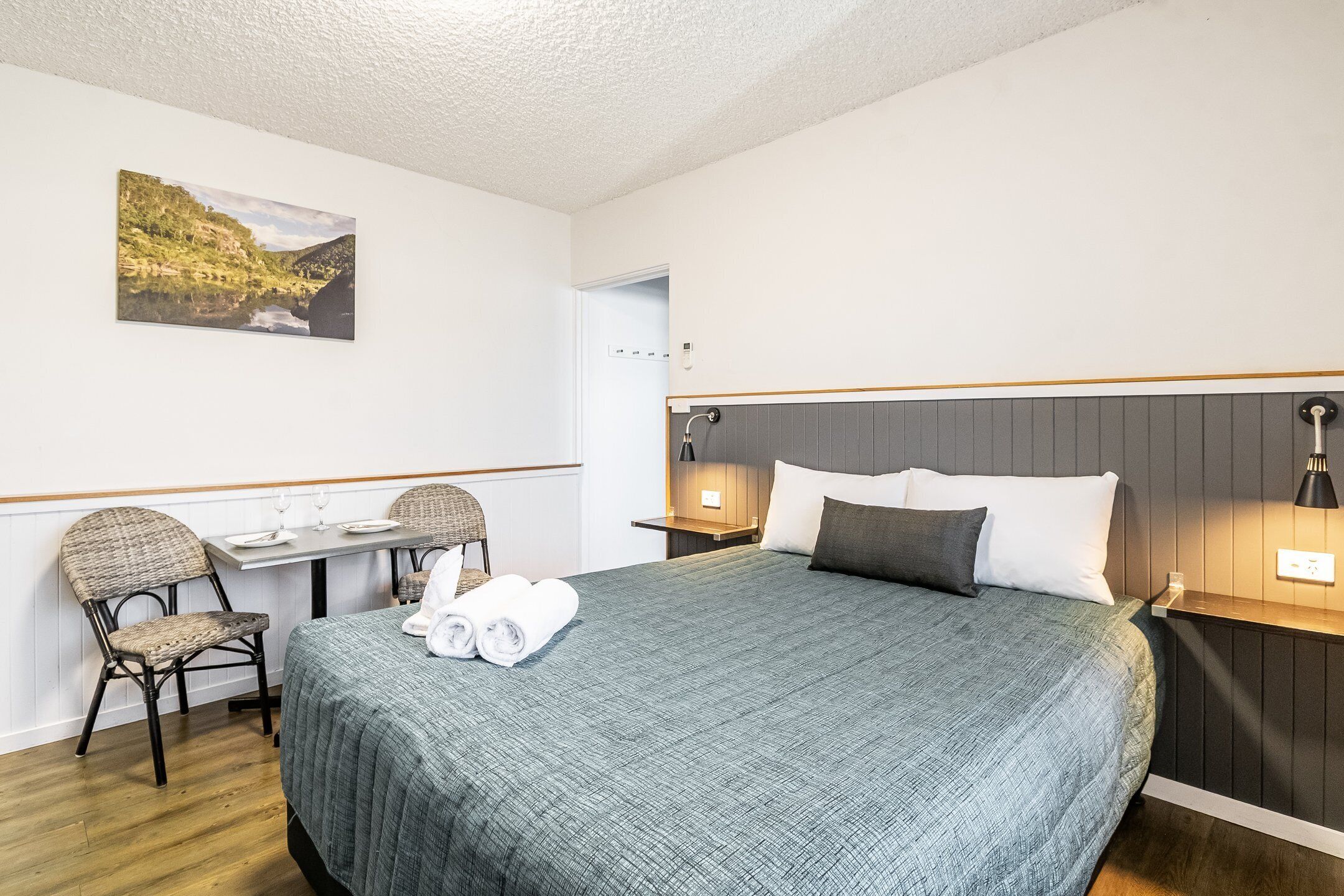 Una habitación de hotel con una cama, un escritorio con una silla, una mesita de noche y una lámpara de pared.