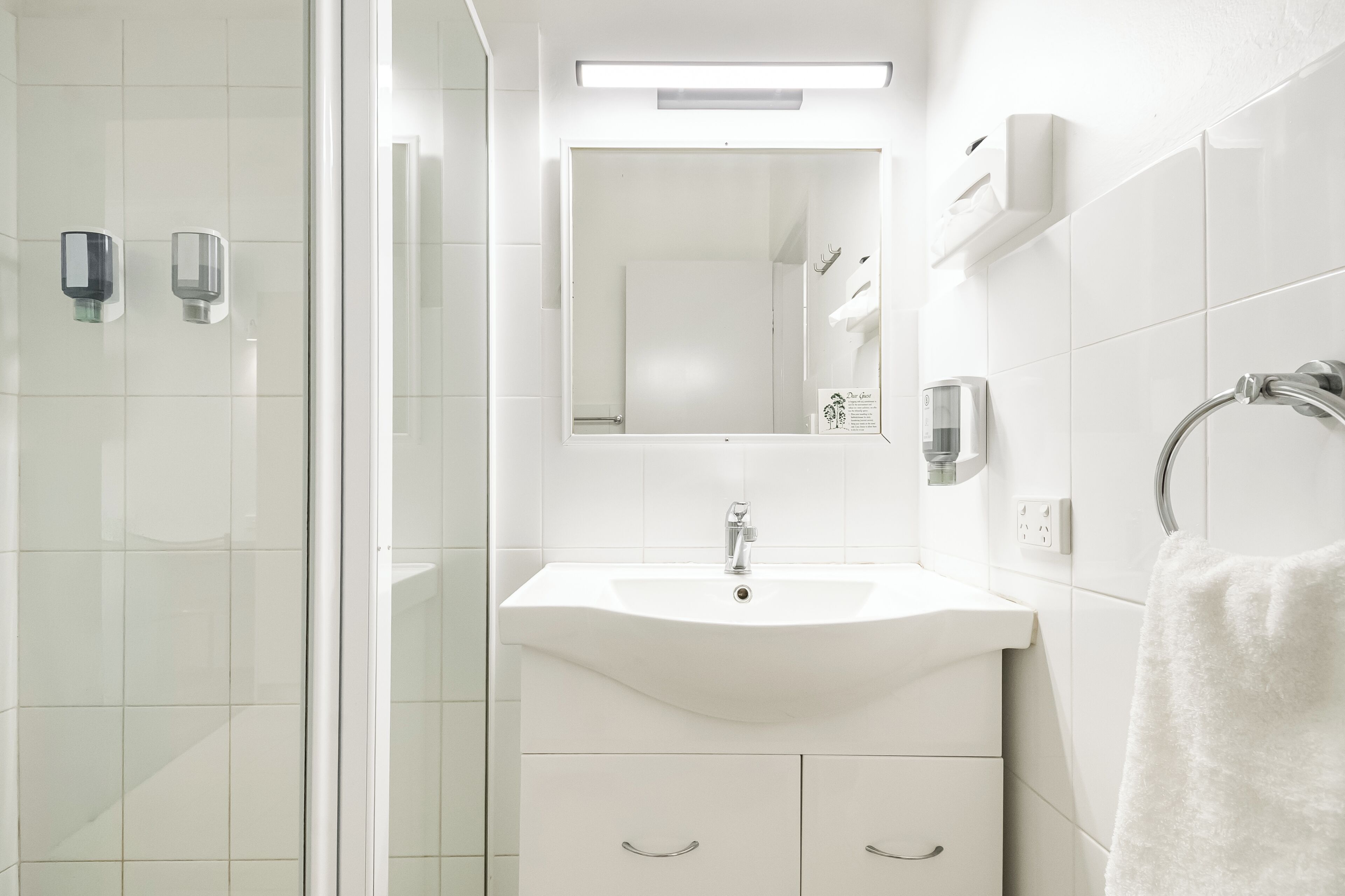 A modern bathroom with a glass shower enclosure, a white sink with a mirror above it, and a towel rack.