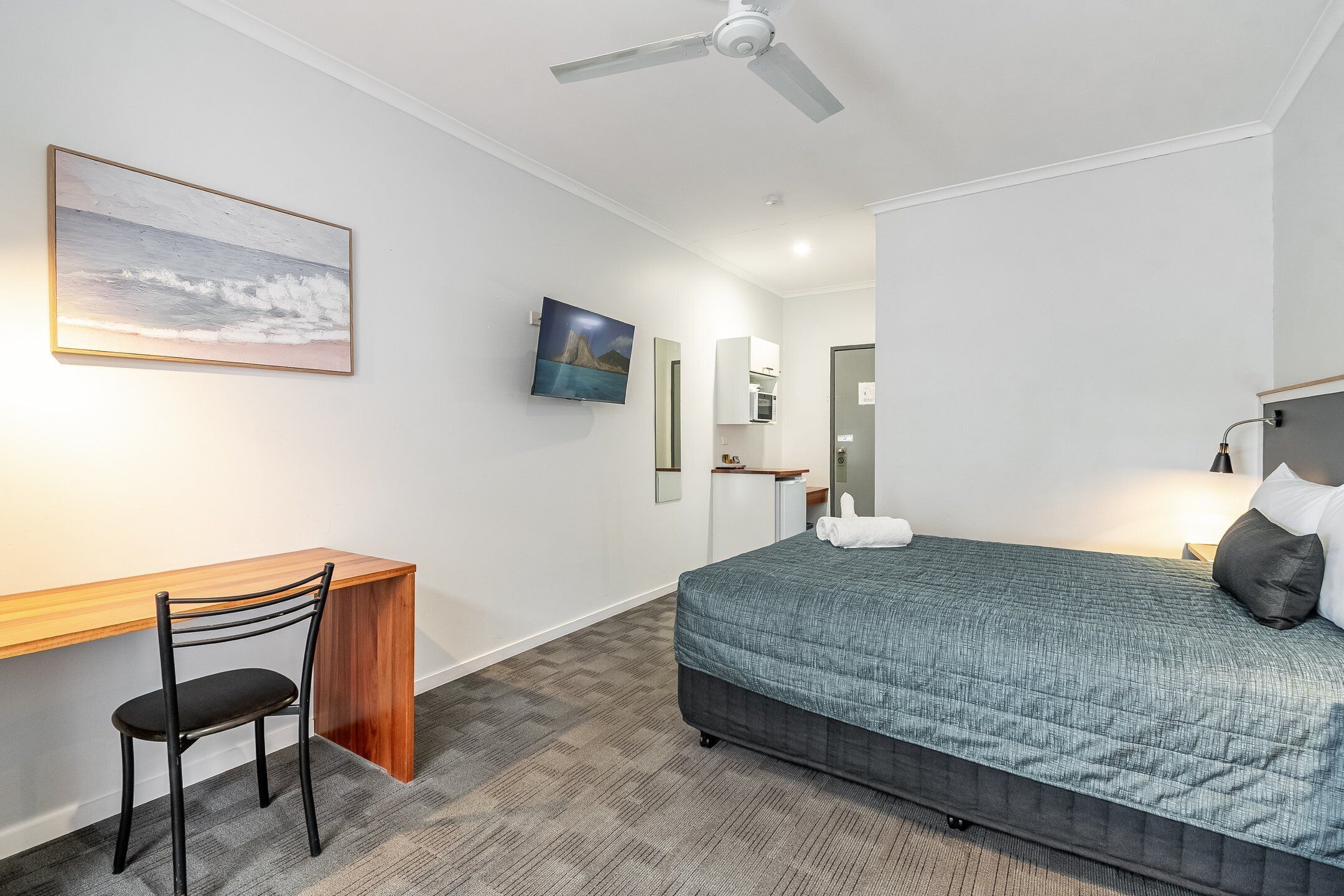 A hotel room with a bed, desk, chair, and a ceiling fan.