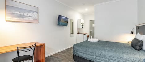 A hotel room with a bed, desk, chair, and a ceiling fan.