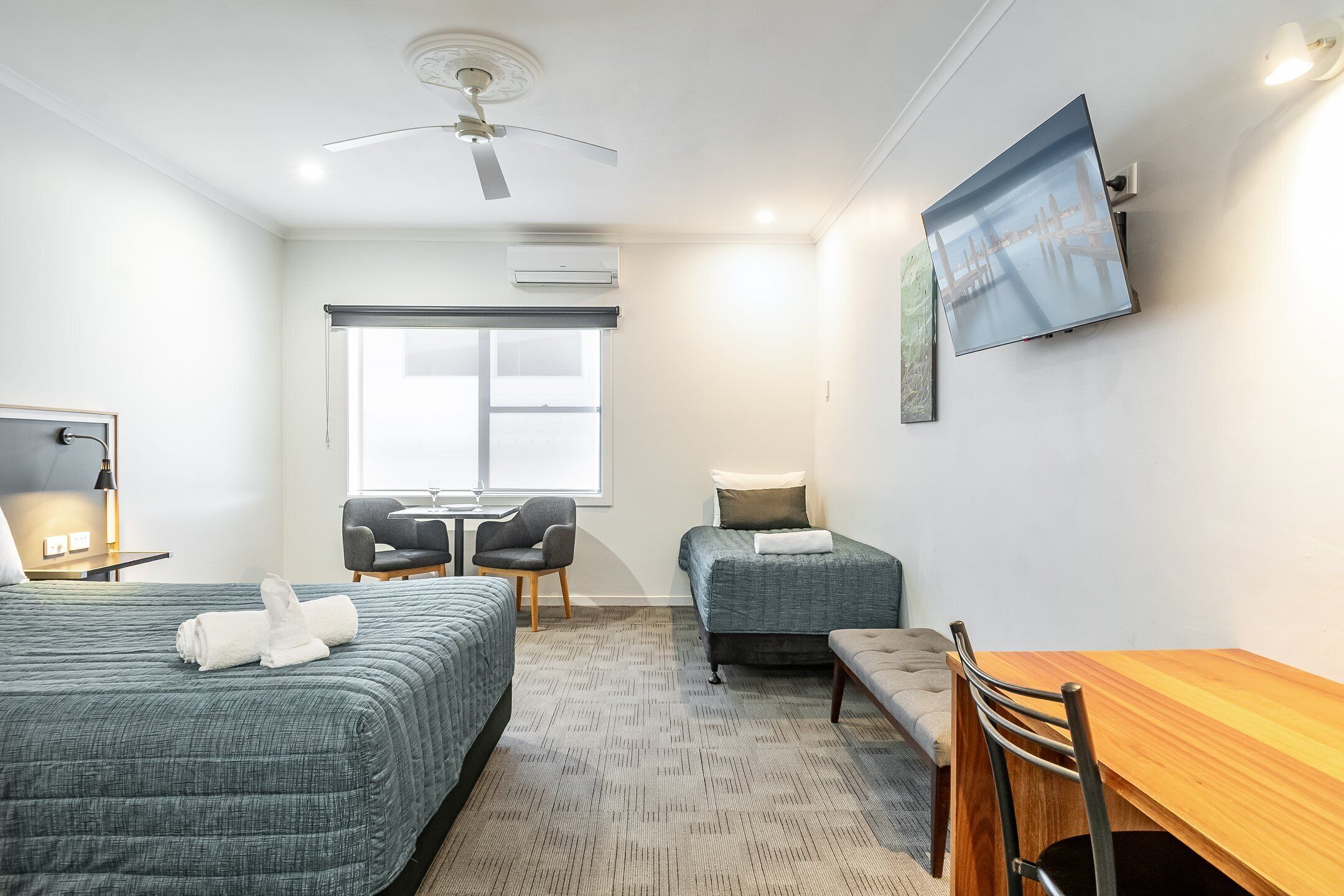 Habitación de hotel con dos camas, un escritorio, una silla, un televisor y una ventana con vistas.