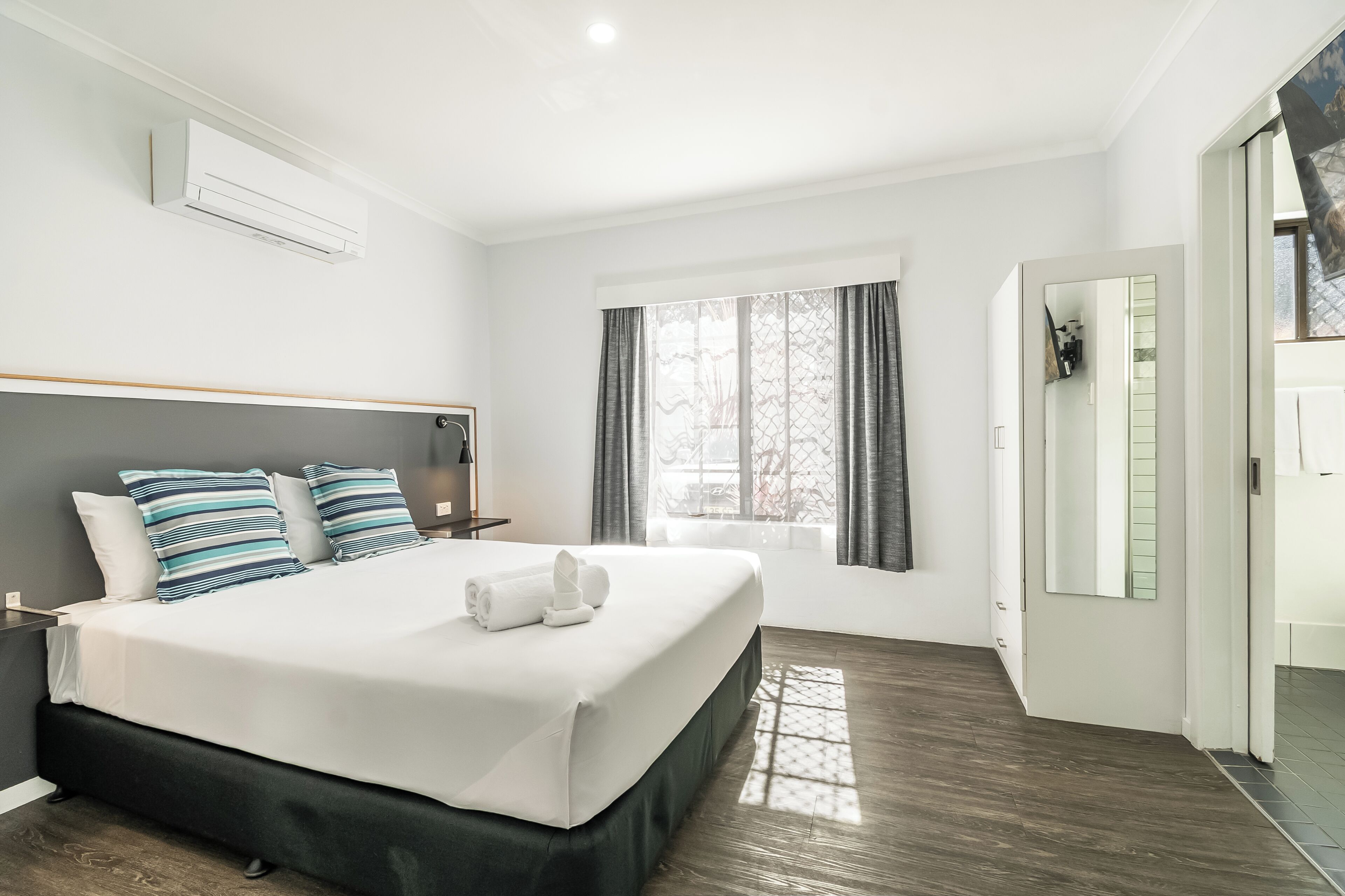 Une chambre d’hôtel moderne avec un grand lit, une table de chevet, une fenêtre avec des rideaux et un appareil de climatisation.